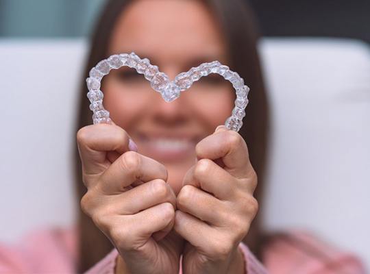 Woman holding Invisalign trays in the shape of a heart