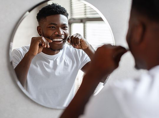 Man smiling while flossing his teeth in bathroom