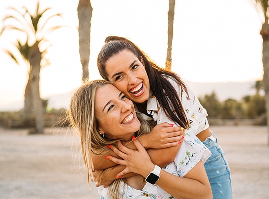 Two friends smiling while hugging outside