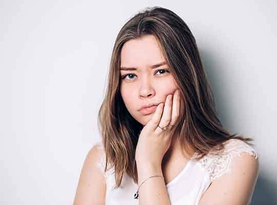 Woman in white shirt rubbing her jaw